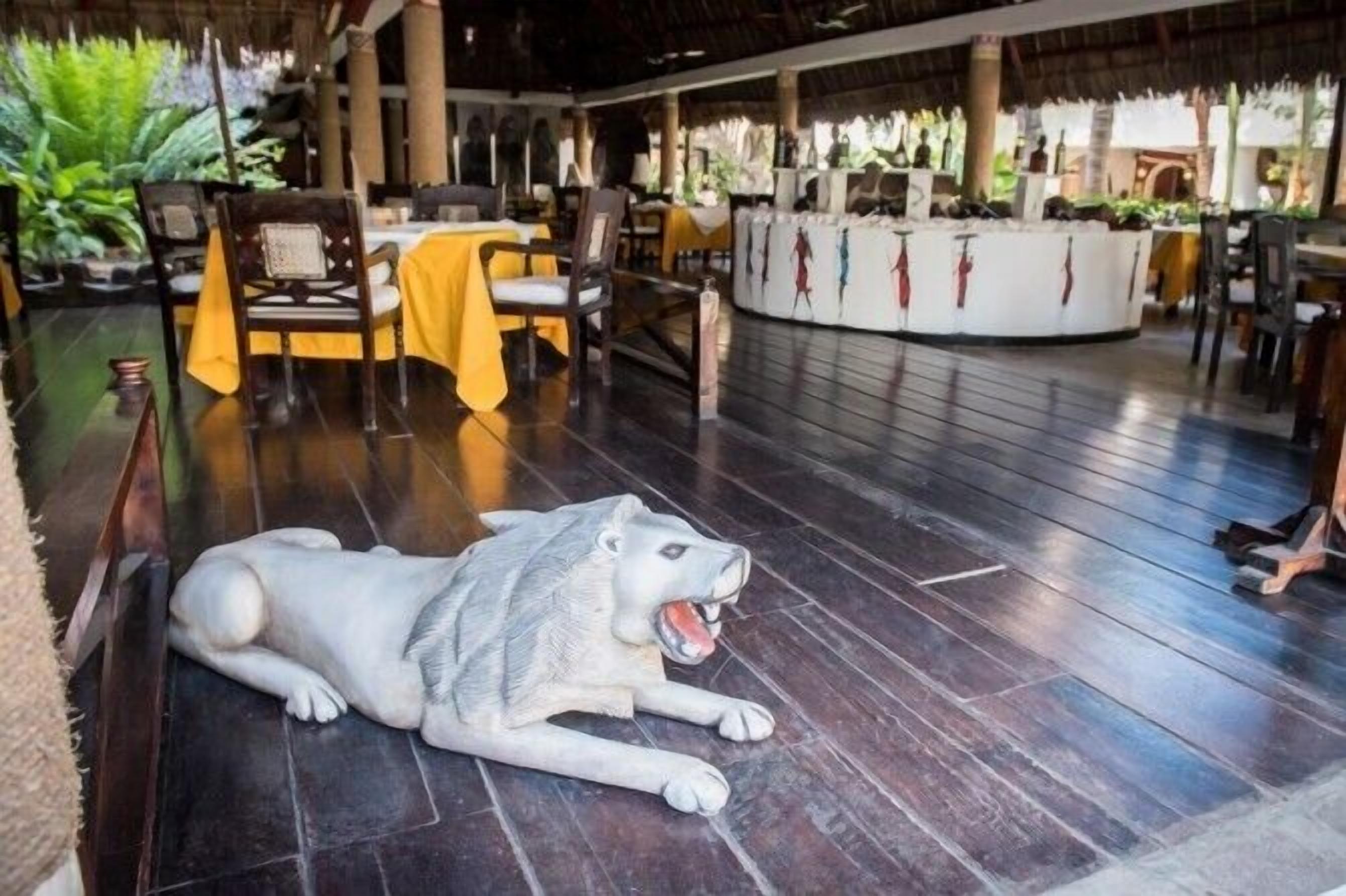 Ein Restaurant mit Holzböden, Tischen mit gelben Tischdecken und einer großen Wolfsskulptur.