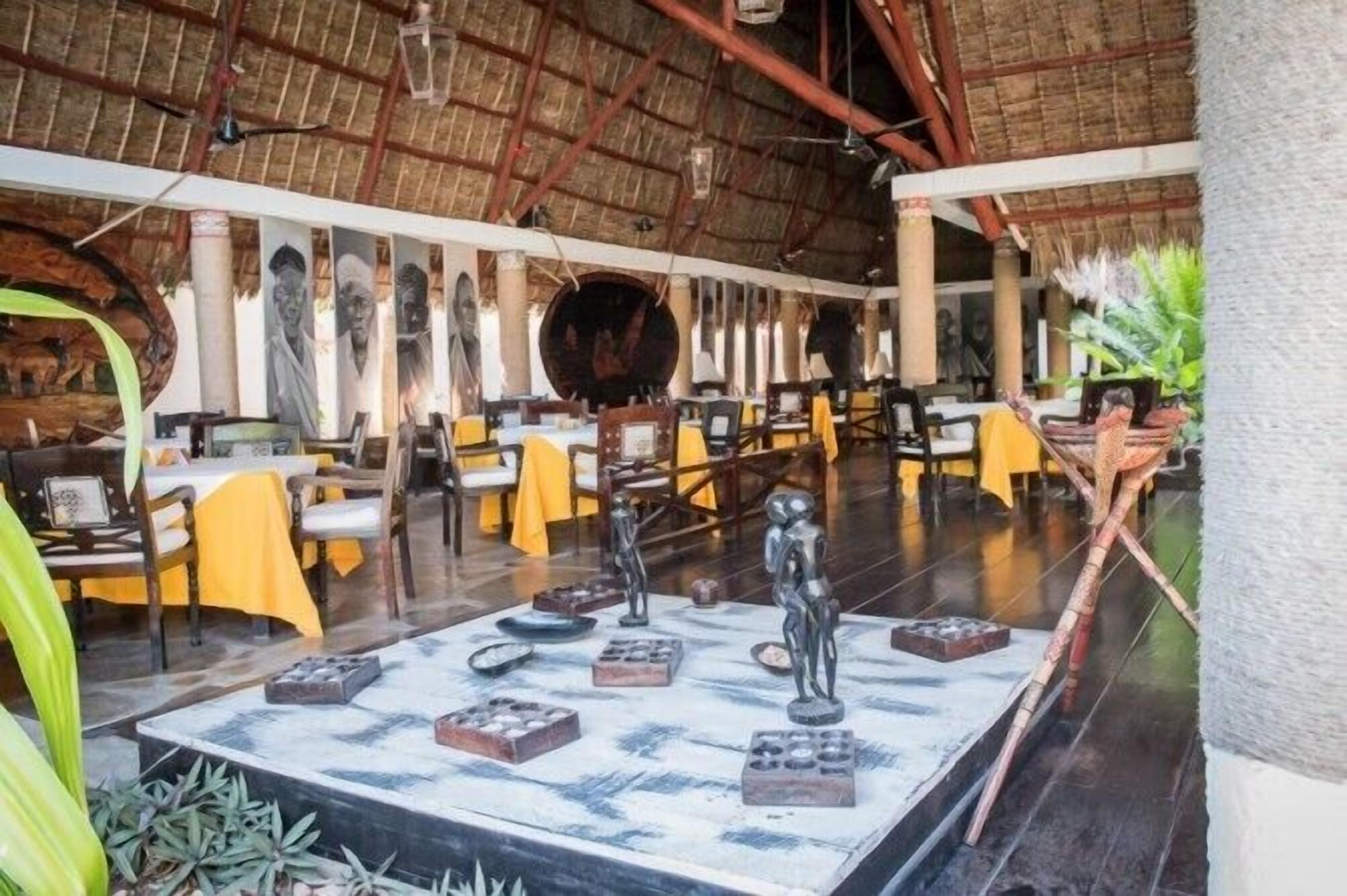 Un restaurant doté d’un toit de chaume, de nappes jaunes et d’une exposition de sculptures au centre de la salle.