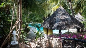A tropical resort with a thatched-roof hut, a swimming pool, and lush greenery. - Scorpio Villas Resort (Malindi)