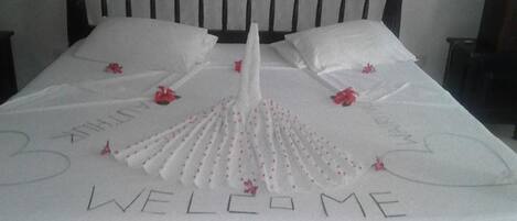 A bed with a white bedspread featuring a fan-like design and the words "WELCOME" and "3" on it.