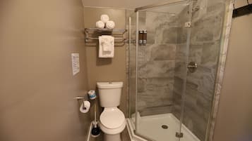 Et badeværelse med brusekabine i glas, toilet og et håndklædestativ med håndklæder.