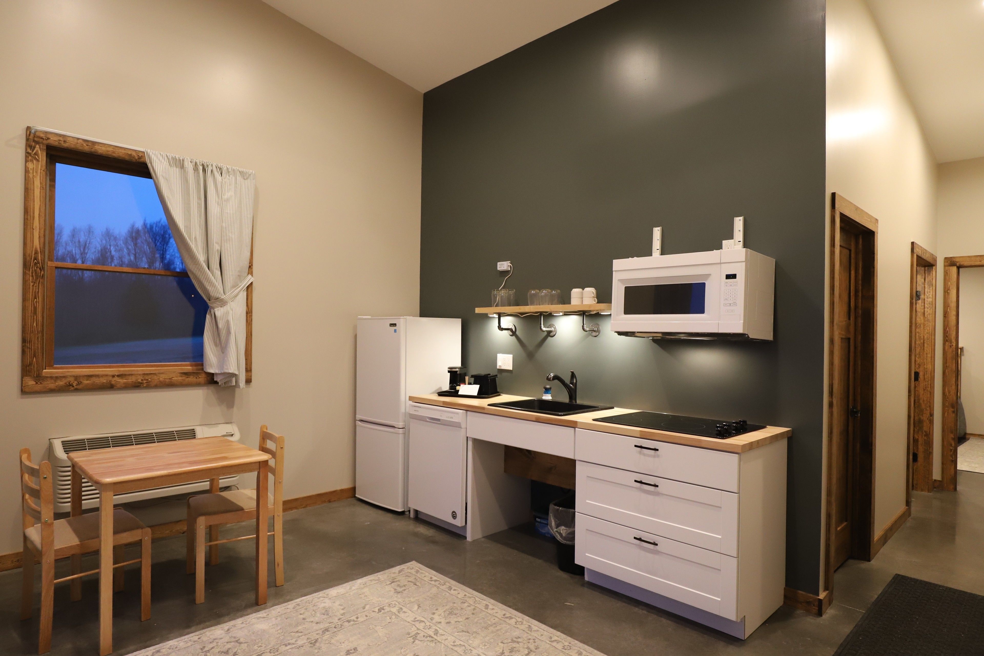 A compact kitchen with a built-in microwave, a sink, and a compact refrigerator. There is a small dining table with chairs.