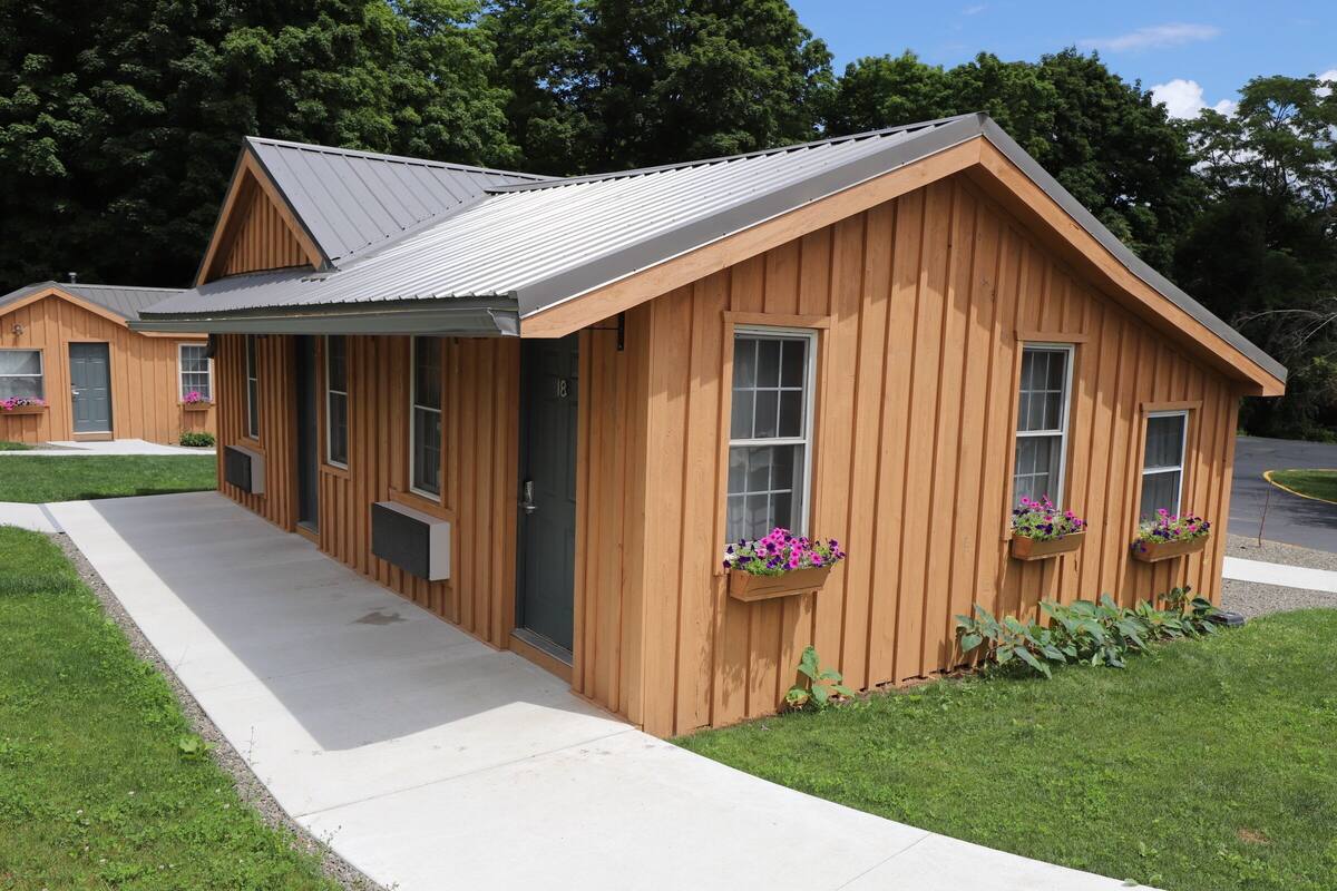 A wooden cabin with a metal roof, a front door, and two windows with flower boxes.