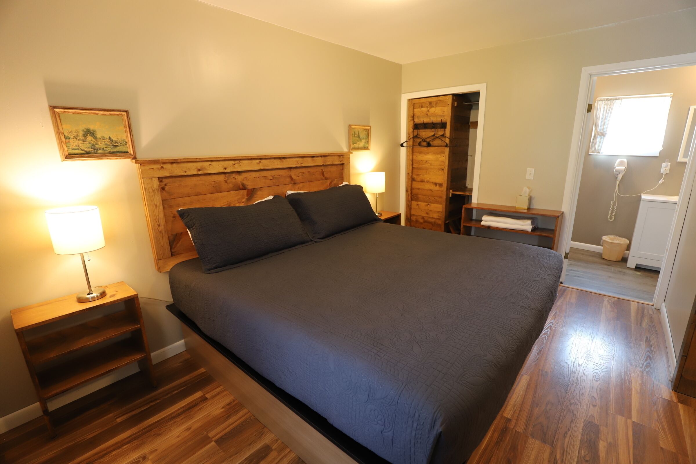 Een slaapkamer met een groot bed, een houten hoofdbord, nachtkastjes met lampen en een houten vloer.