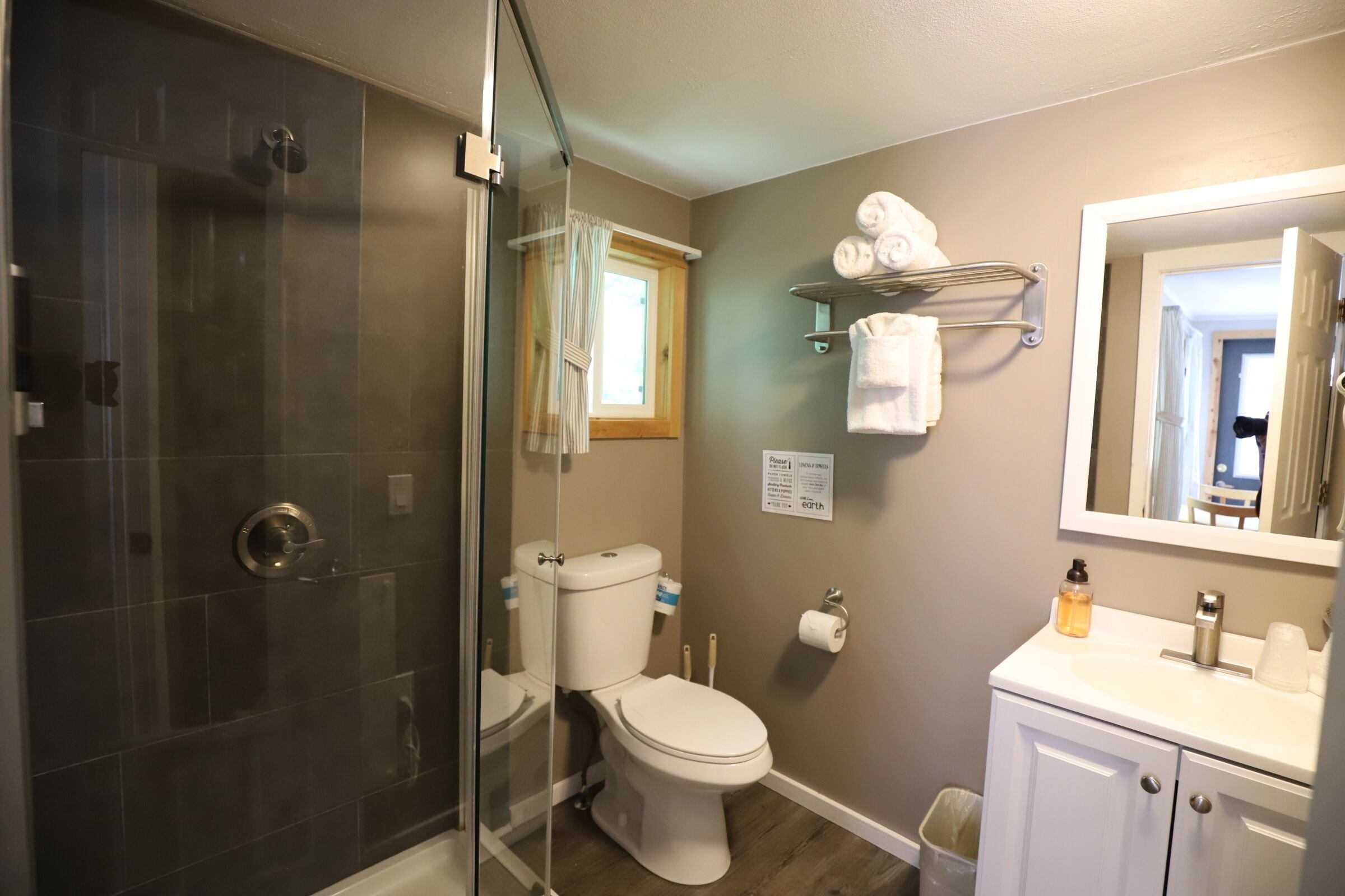 Un baño con ducha envuelta en vidrio, inodoro, lavabo con espejo y toallero.