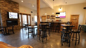 Un restaurante con pared de piedra, televisor sobre la chimenea y una zona de bar con taburetes y mostrador.