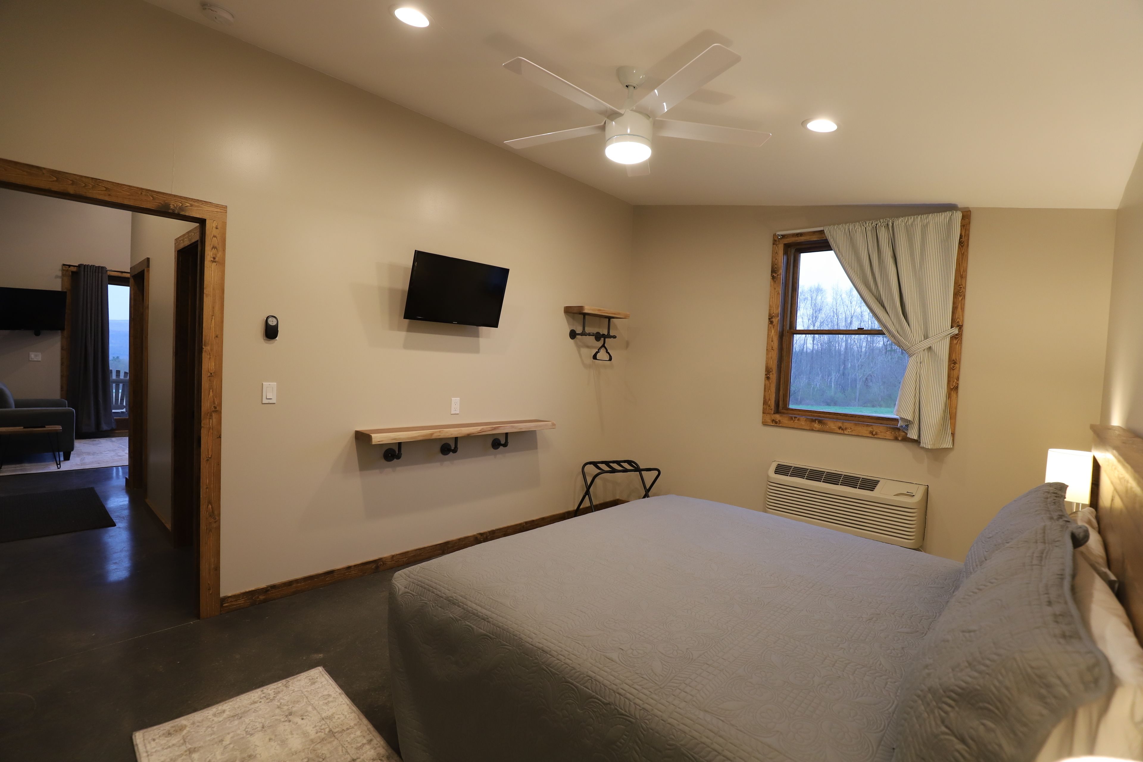 A bedroom with a bed, a ceiling fan, a TV, a window with curtains, and a small shelf.