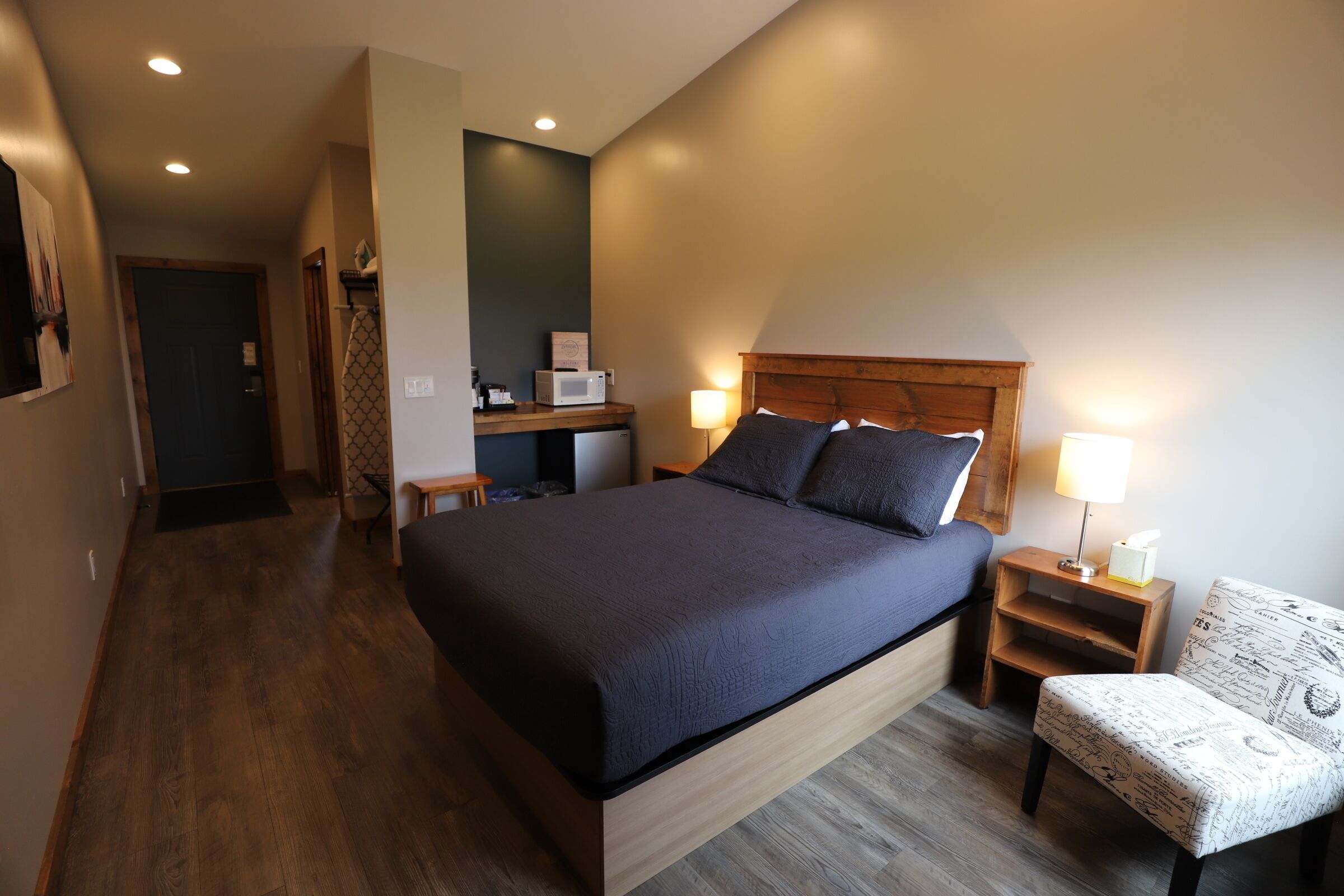 Una habitación de hotel moderna con una cama grande, mesitas de noche, una silla y un escritorio con microondas.