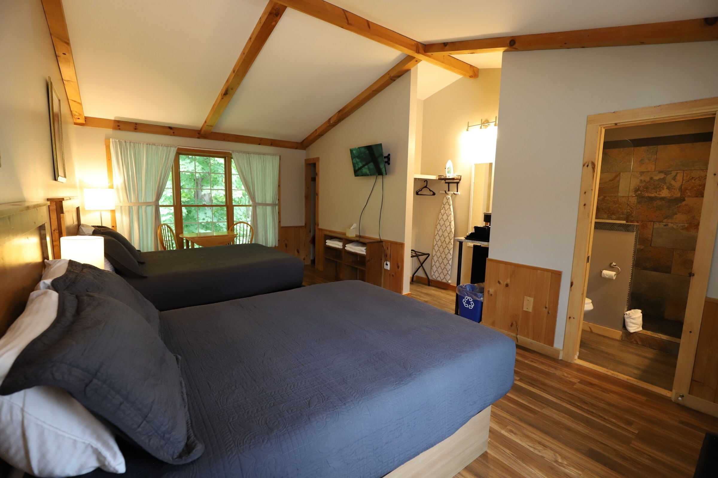 Une chambre à coucher avec un lit, un téléviseur fixé au mur et un espace douche visible à travers une porte ouverte.