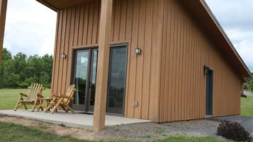 A wooden cabin with a covered porch, two Adirondack chairs, and a sliding glass door.