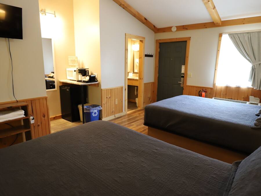 A hotel room with two beds, a TV mounted on the wall, a desk with a computer, and a window with curtains.