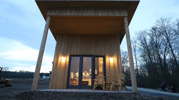 Una cabaña de madera con un porche cubierto, una zona de comedor y una cocina visibles a través de puertas correderas de cristal.