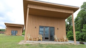 Un edificio moderno con techo plano y grandes puertas correderas de vidrio. Varias sillas de madera están dispuestas en el exterior.