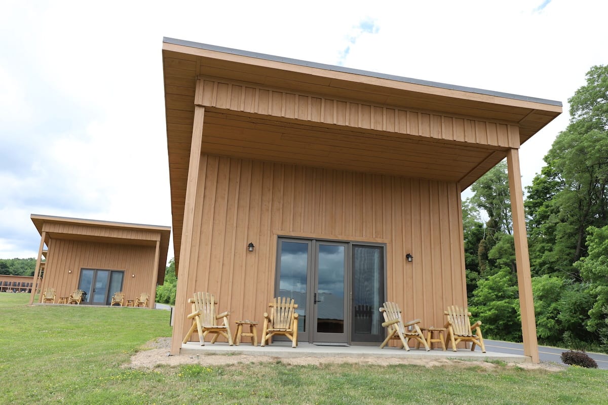 A modern building with a flat roof and large sliding glass doors. There are several wooden chairs arranged outside.