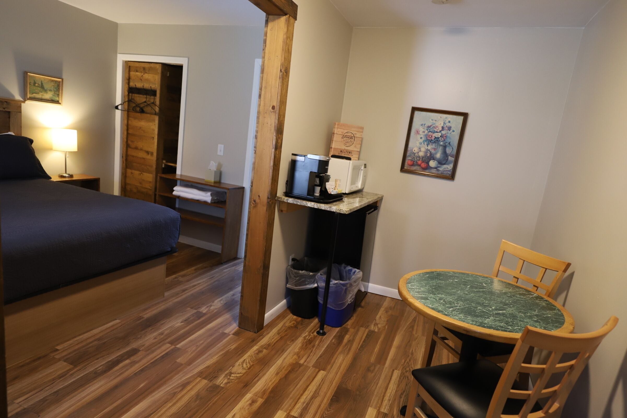 A room with a bed, a table with chairs, a microwave, a coffee maker, and a trash bin.