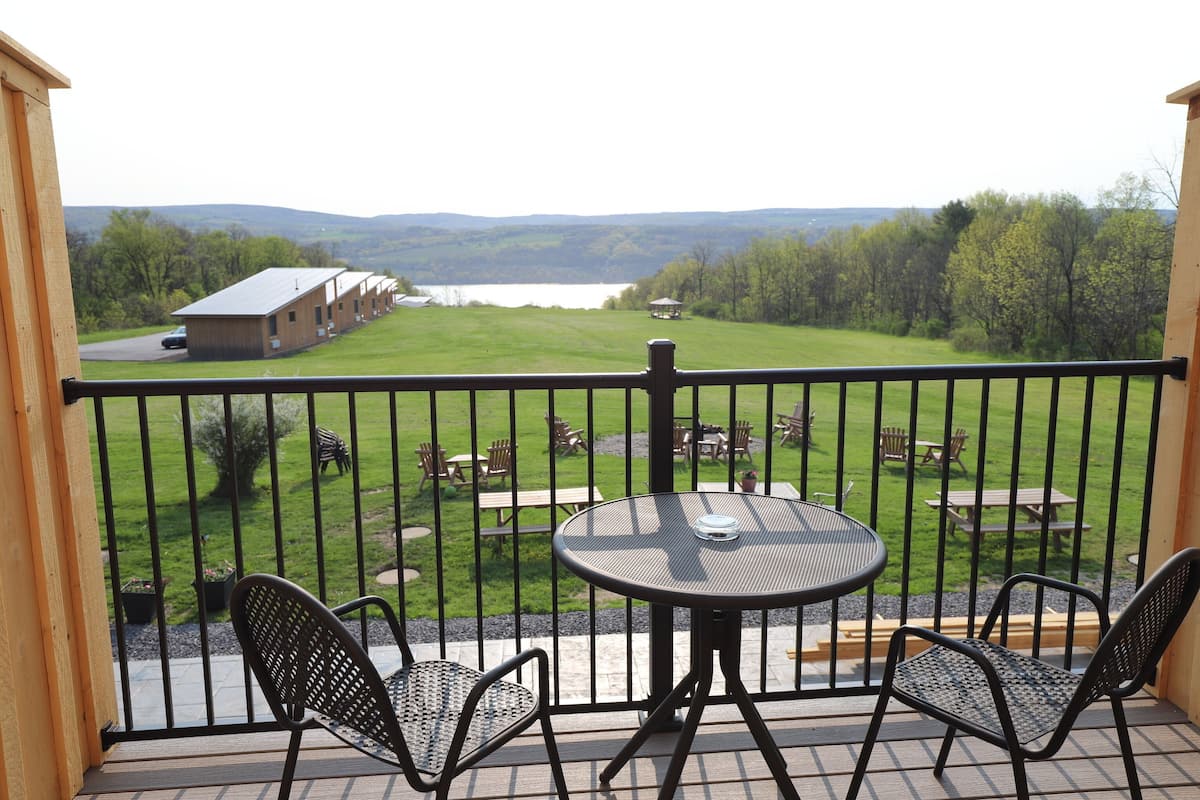 A balcony with a view of a grassy area with picnic tables and a building in the distance.