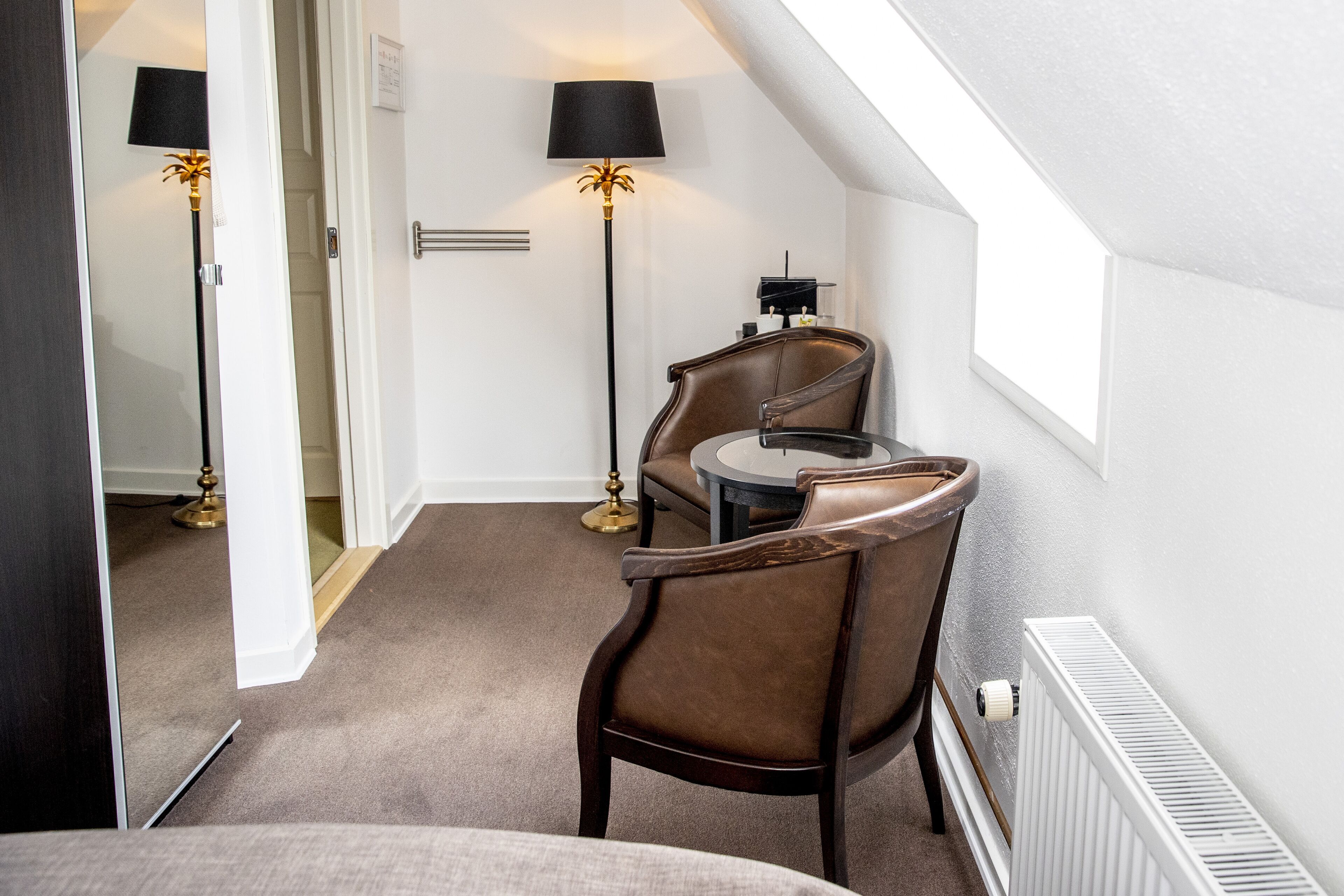 A room with a bed, a chair, a table, a lamp, and a radiator.