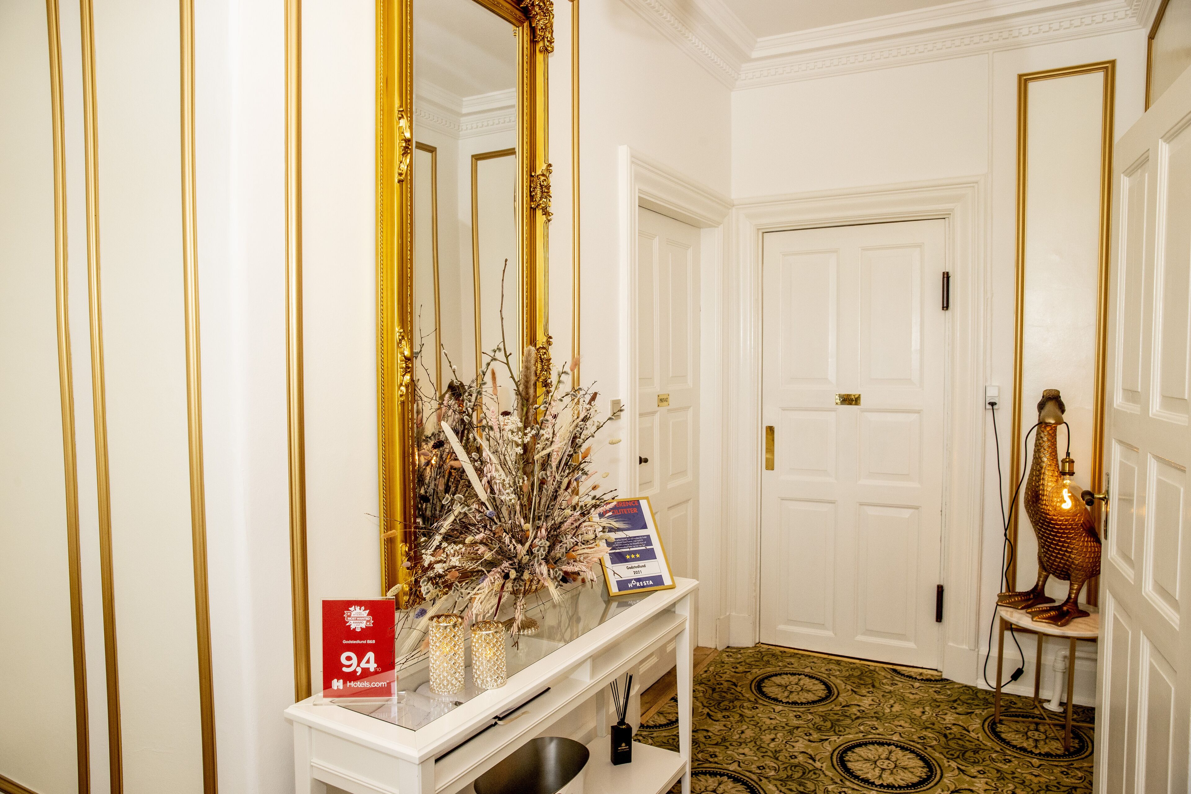 A hallway with a white console table, a large mirror, a decorative vase, and a sign indicating a 94% rating.