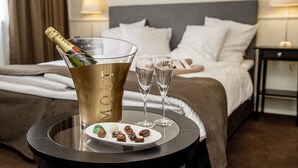 A bed with white linens, a bedside table with a bottle of champagne and glasses, and a plate with chocolates. - Godstedlund B&B (Oster Ulslev)