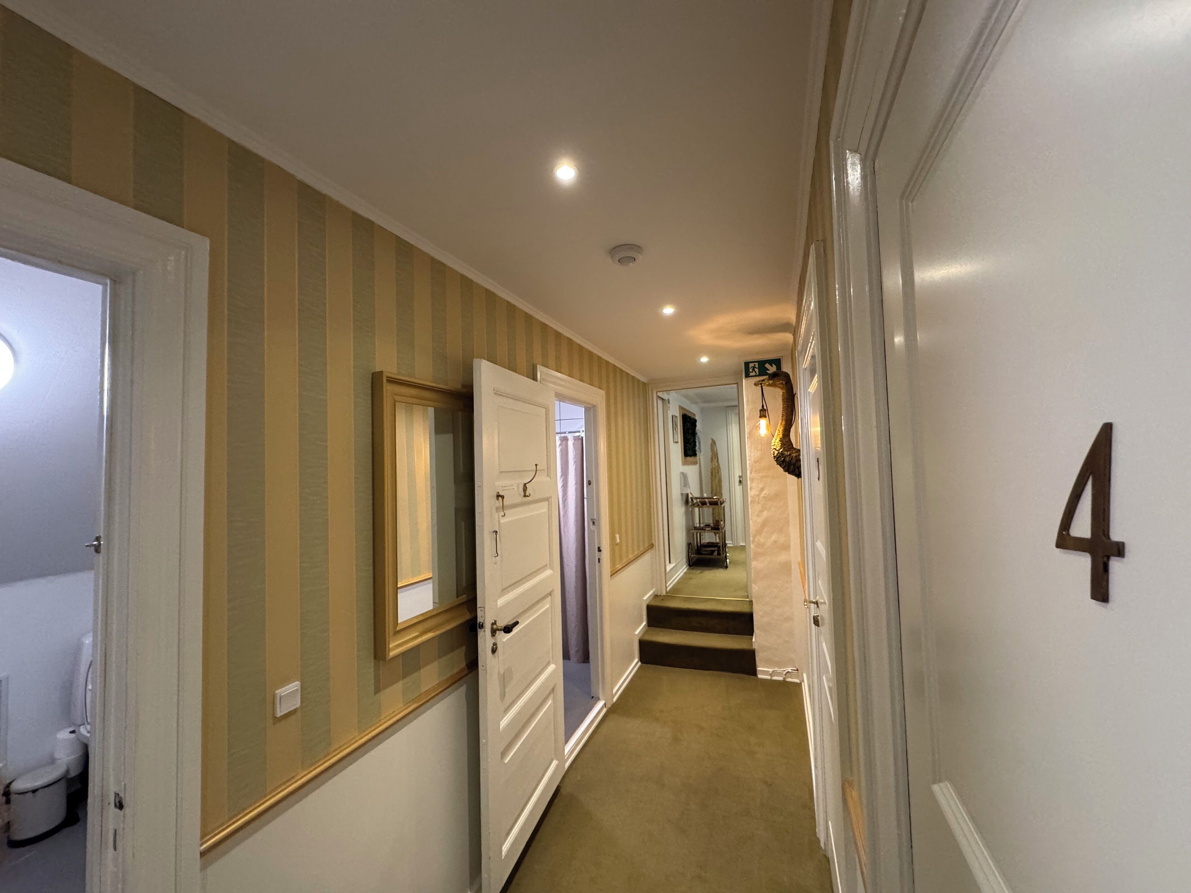 A hallway with striped wallpaper, a door with a number '4' sign, and a staircase leading to another room.