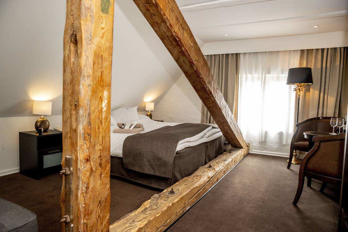 A hotel room with a bed, a nightstand, a chair, and a table with a lamp.