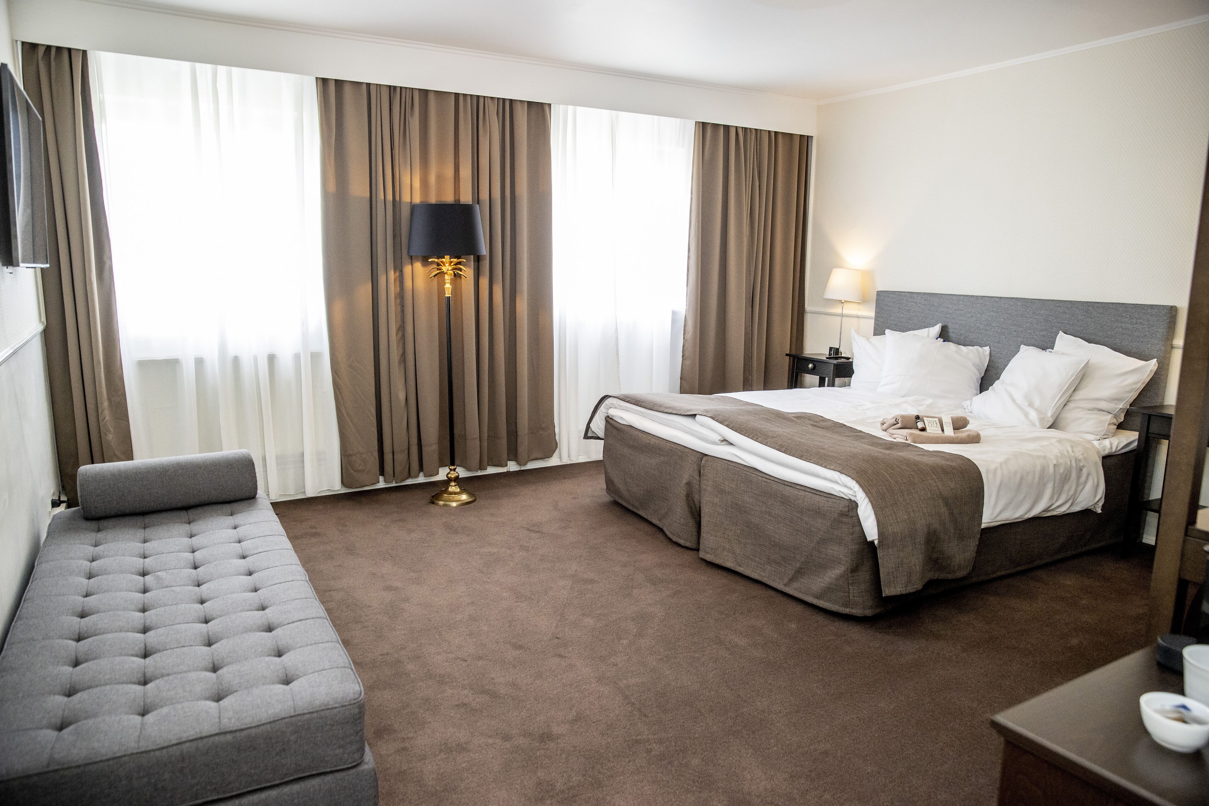 A hotel room with a large bed, a sofa, a nightstand, and a lamp.