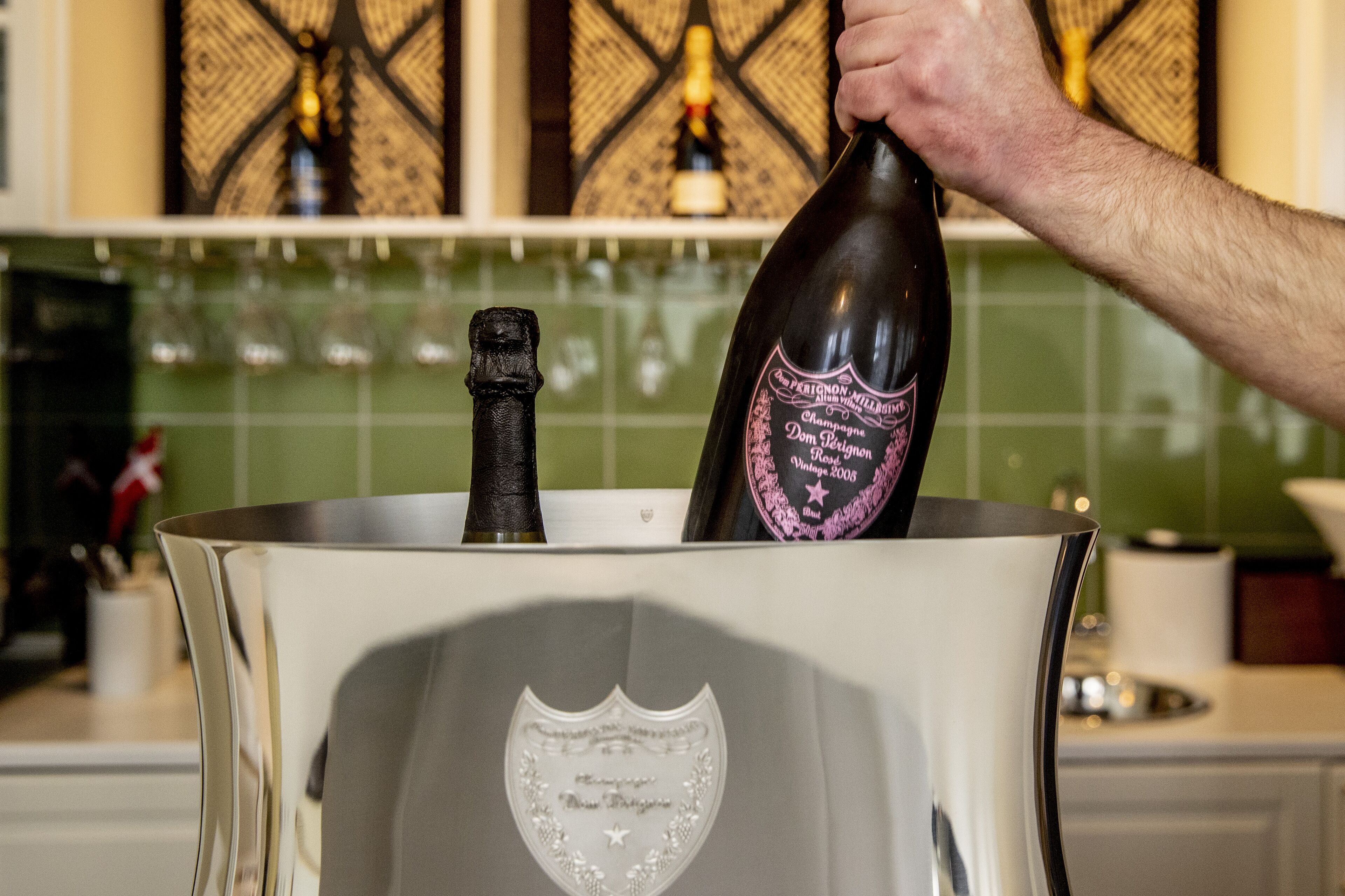 A bottle of wine being poured into a large, metallic container with a decorative emblem.