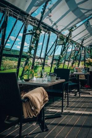 Un comedor estilo invernadero con una mesa para dos, sillas alrededor y vistas a un paisaje verde a través de amplios paneles de vidrio.