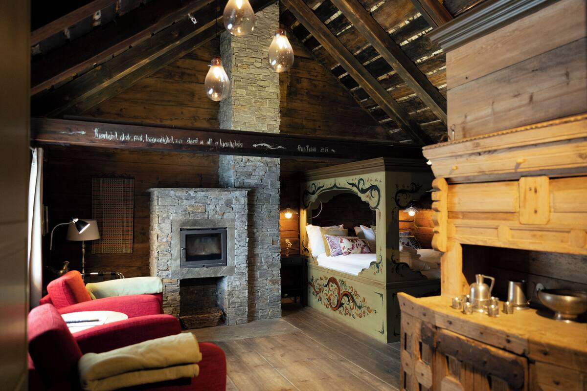 Een rustiek interieur met een stenen openhaard, houten balken en een bed met decoratief hoofdeinde.