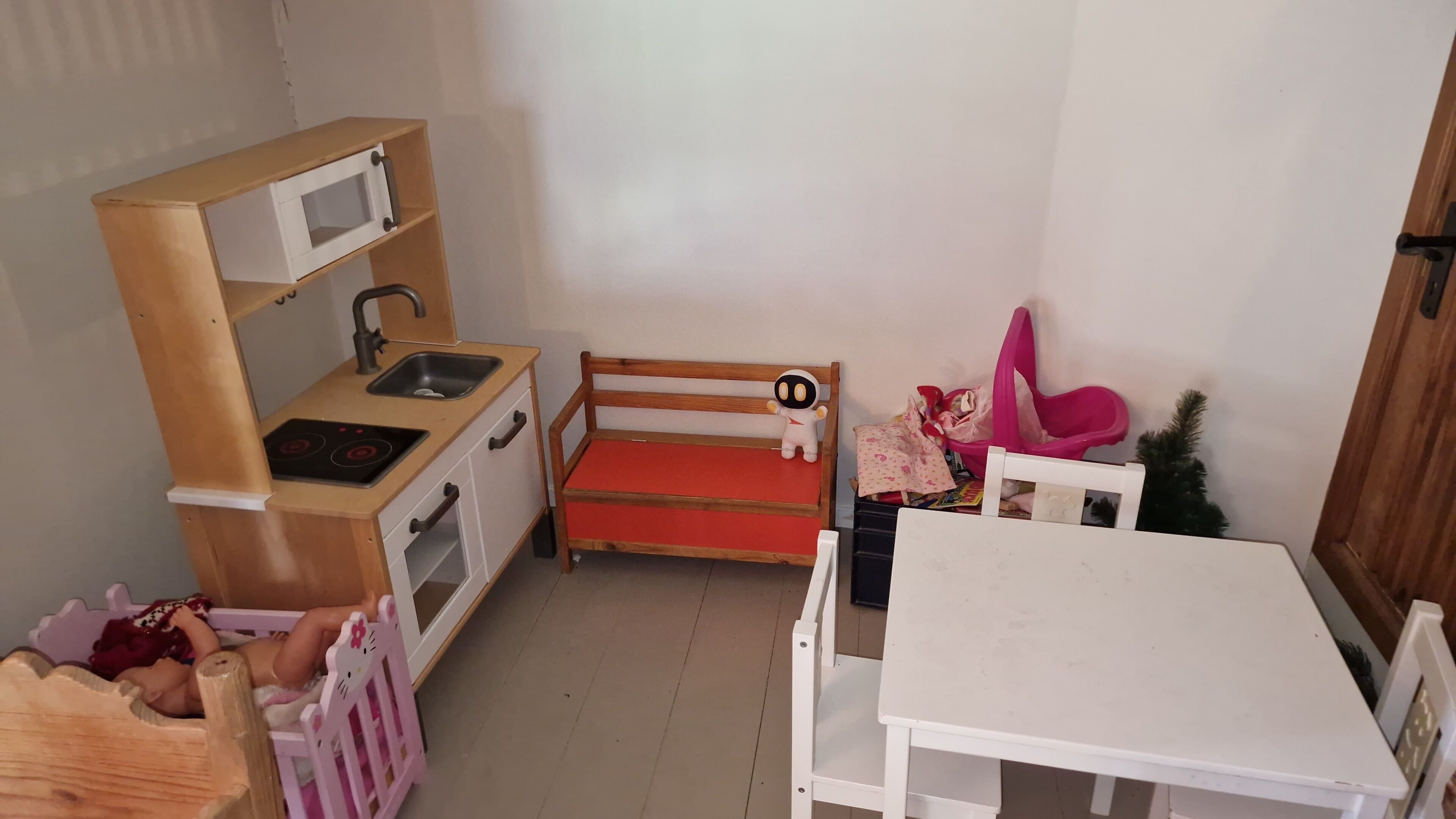 Un cuarto infantil con una pequeña cocina americana, una cama y una mesa blanca.