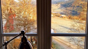 Una ventana con vista a un paisaje rural, una lámpara de escritorio y una piña en el alféizar.