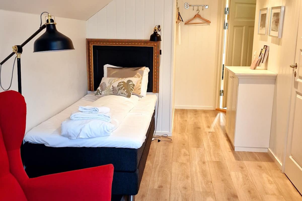 Een slaapkamer met een bed, een rode stoel, een bureau, een lamp en een gang naar een badkamer.