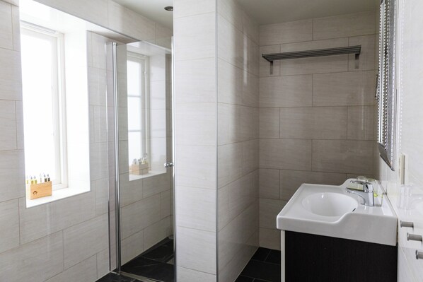A modern bathroom with a glass shower door, a white sink, and a window with a wooden shelf. - Store Ringheim Hotell og Restaurant (Voss)