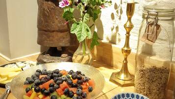 A table with a fruit salad, bowls of jam, a candle, a statue, and a vase with flowers.