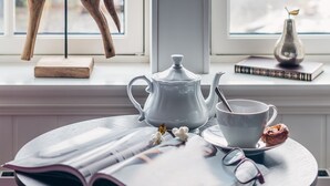 Una habitación acogedora con un caballo balancín de madera, una tetera blanca, una taza y un libro en el alféizar de una ventana.