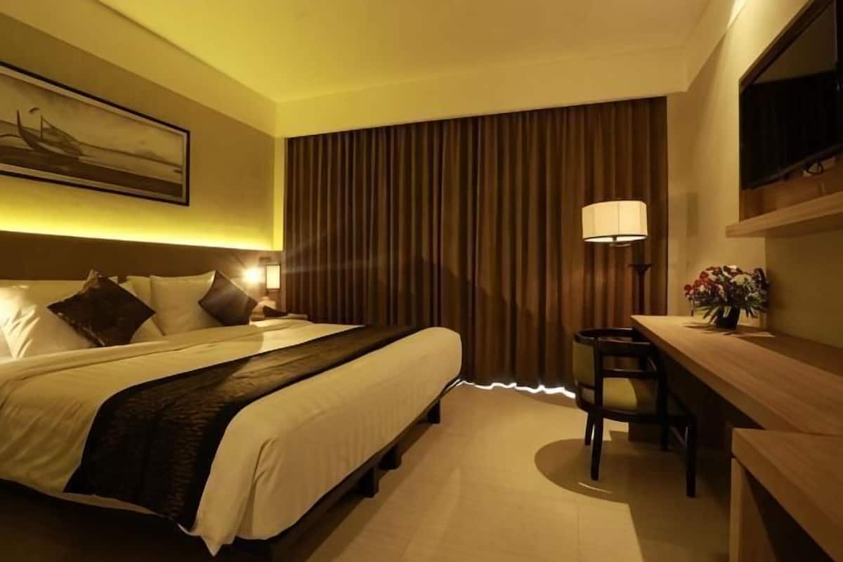 Habitación de hotel con cama, escritorio, lámpara y un cuadro en la pared.