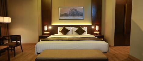 Una habitación de hotel con una cama grande, una mesita de noche, una lámpara, una silla y un cuadro en la pared.