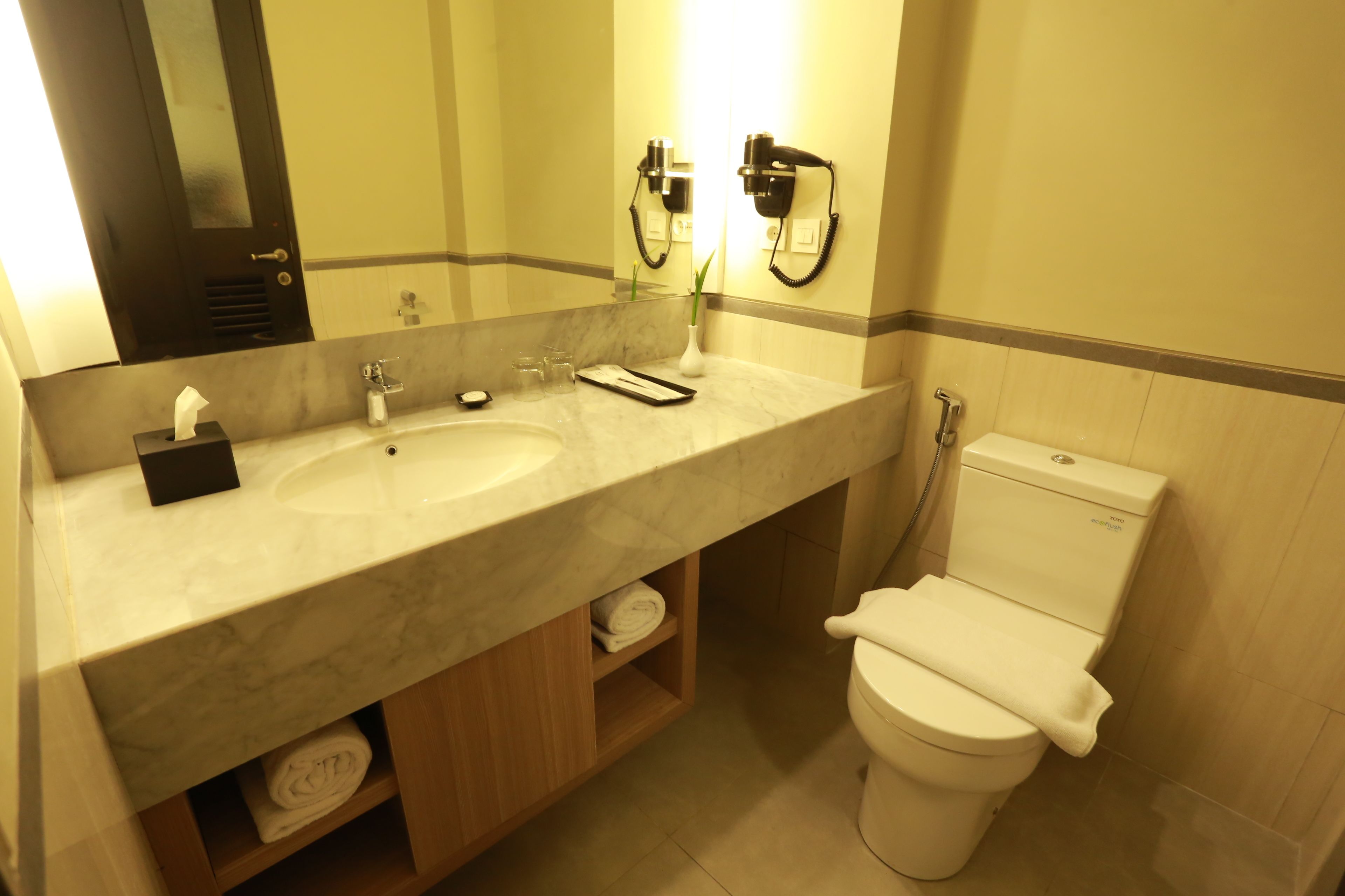 A bathroom with a marble sink, two hair dryers, a toilet, and a mirror.