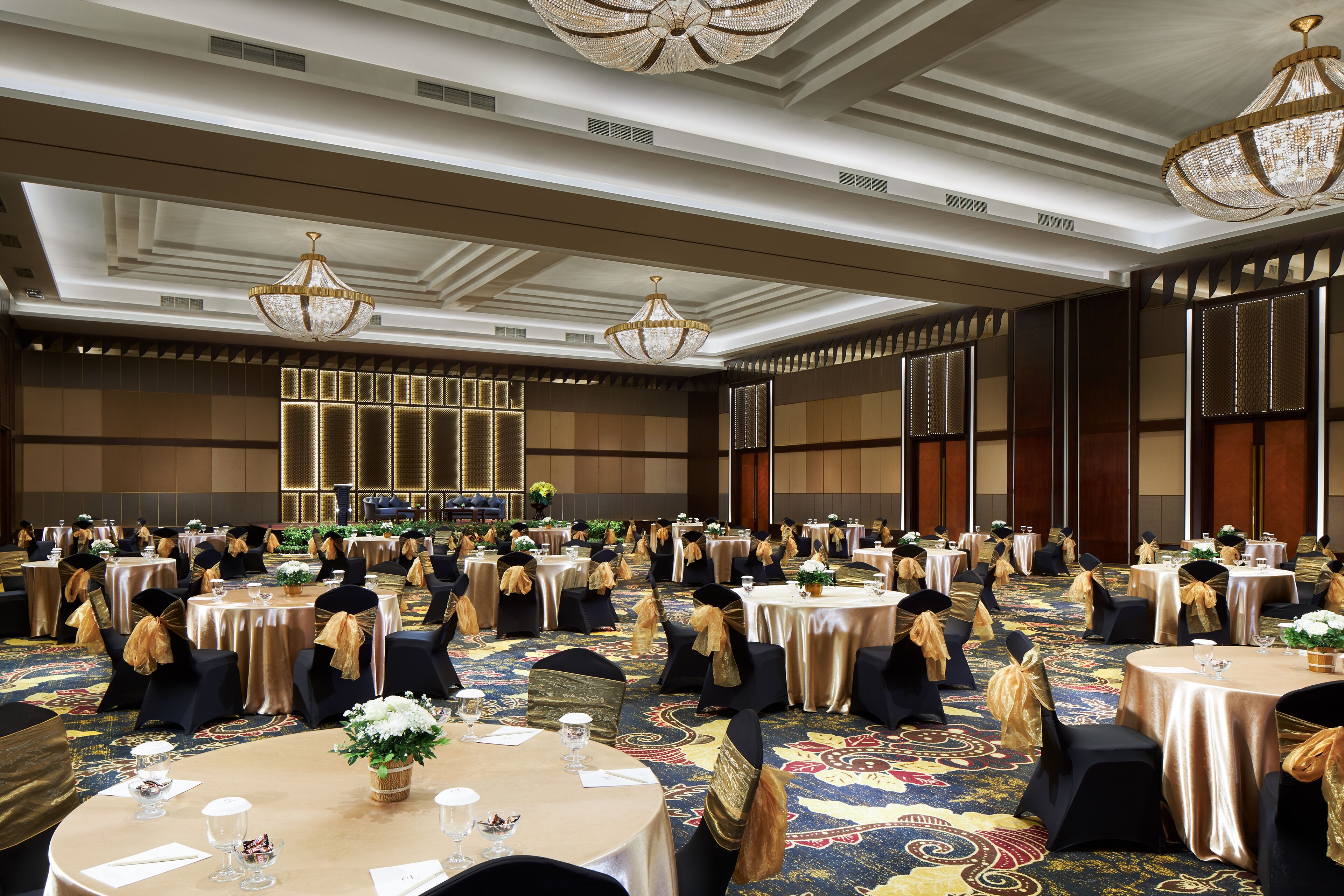 A banquet hall with round tables, black chairs, and gold sashes.
