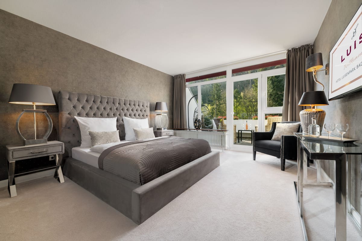 Een moderne hotelkamer met een groot bed, een bureau, een stoel en een groot raam met uitzicht op de omgeving.