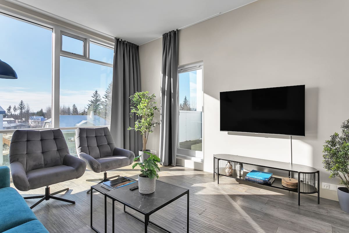 Una sala moderna con un televisor grande, asientos cómodos, una mesa de centro y vistas de la ciudad.