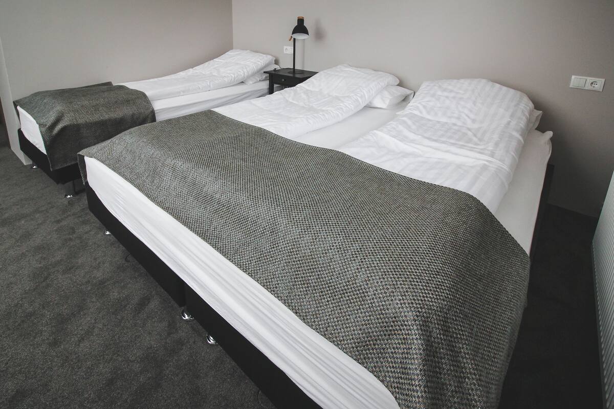 Habitación de hotel con dos camas individuales, una cama grande y una mesita de noche con lámpara.