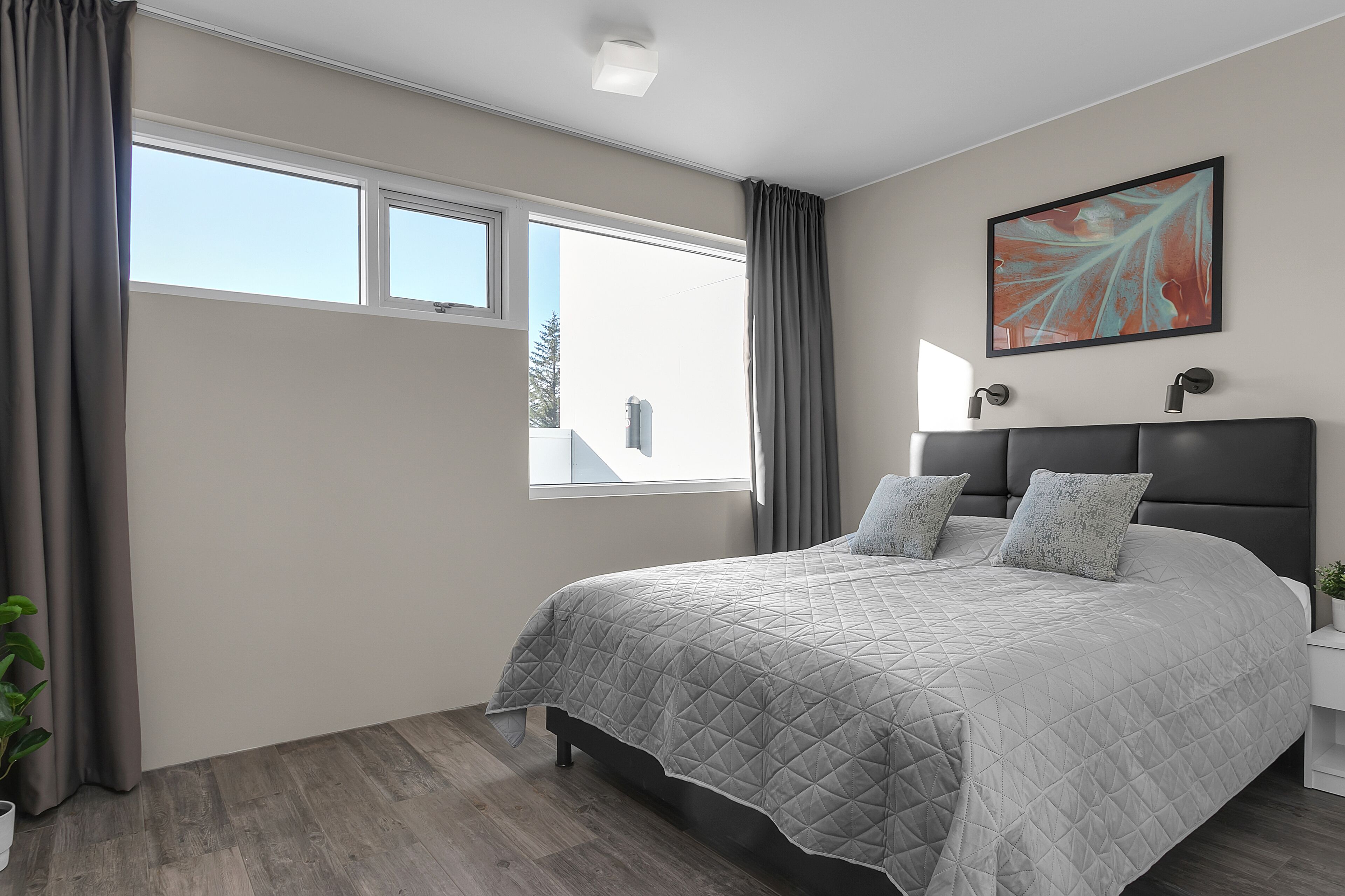 Quarto moderno com uma cama grande, duas mesas de cabeceira, um vaso de planta e uma janela com cortinas.
