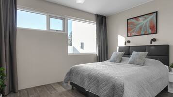 Quarto moderno com uma cama grande, duas mesas de cabeceira, um vaso de planta e uma janela com cortinas.