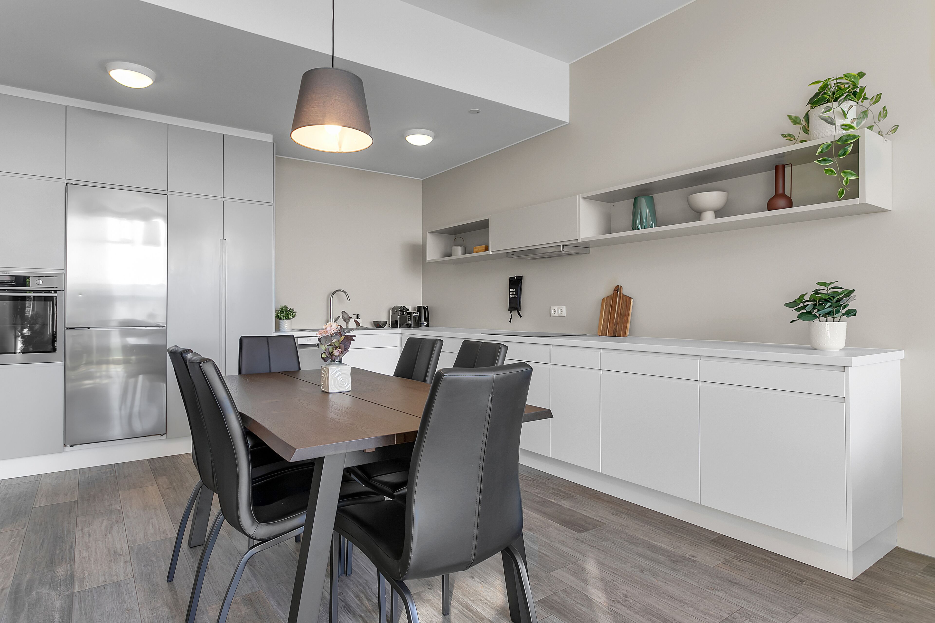 Una cocina moderna con armarios blancos, un refrigerador de acero inoxidable y un comedor con una mesa de madera y sillas negras.