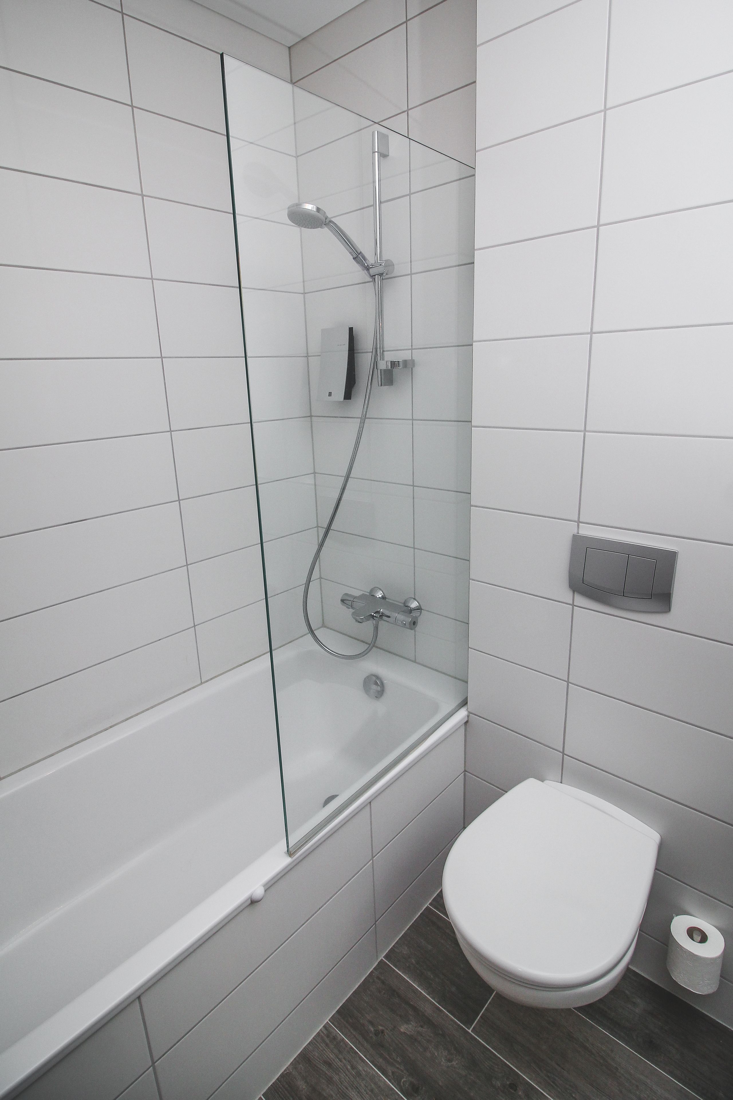 A modern bathroom with a glass-enclosed shower, a white toilet, and a visible toilet paper roll.