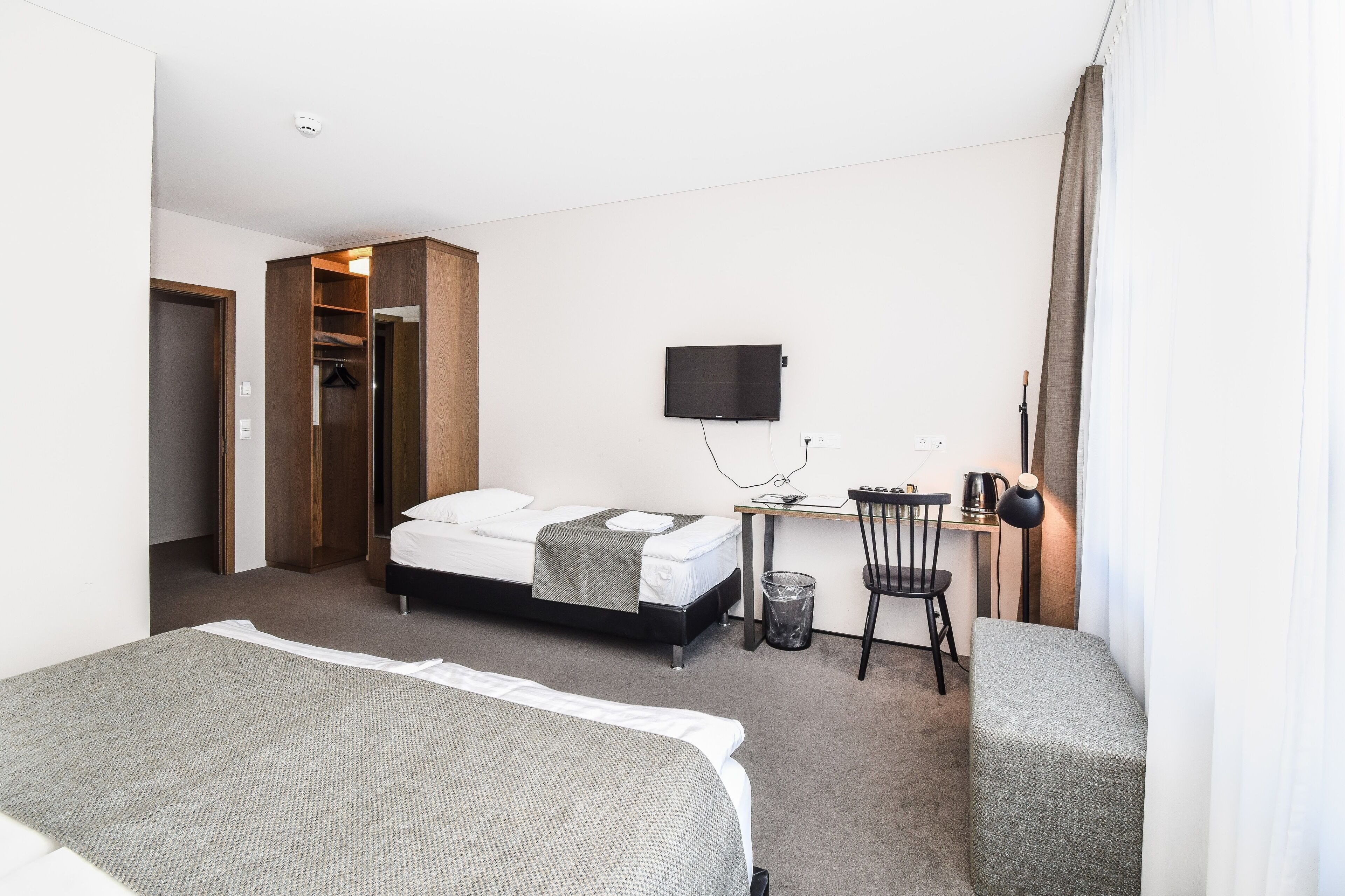 Ein Hotelzimmer mit einem Bett, einem Schreibtisch mit Computer, einem Sessel, einem Fernseher und einem Kleiderschrank.