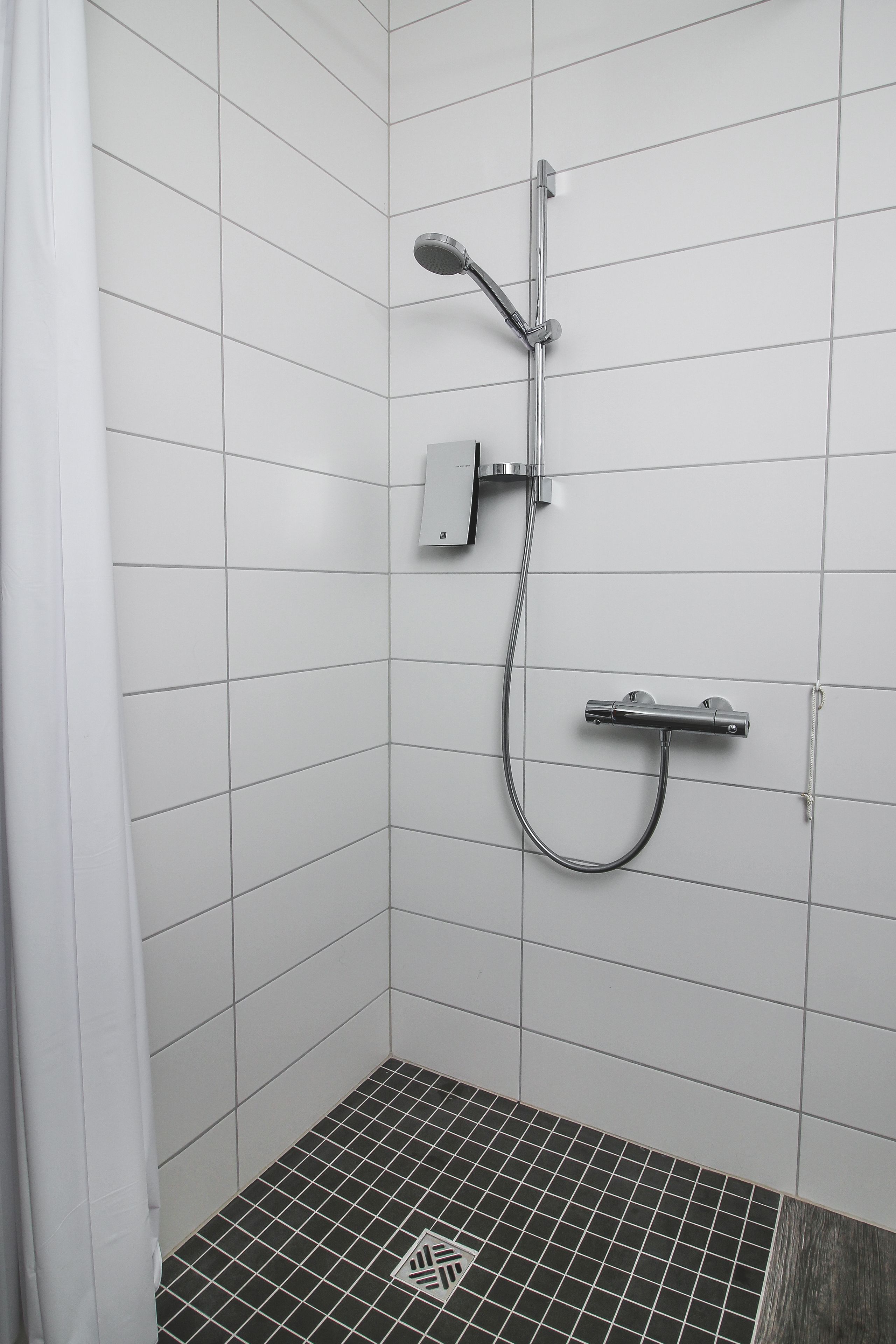 A shower area with white tiled walls and a black tiled floor.