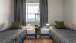 Ein Doppelzimmer mit zwei Betten, einem Fenster mit Vorhängen, Nachttischlampen und einer Topfpflanze.
