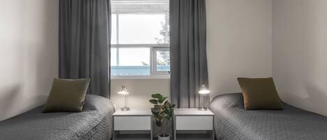 Ein Doppelzimmer mit zwei Betten, einem Fenster mit Vorhängen, Nachttischlampen und einer Topfpflanze.